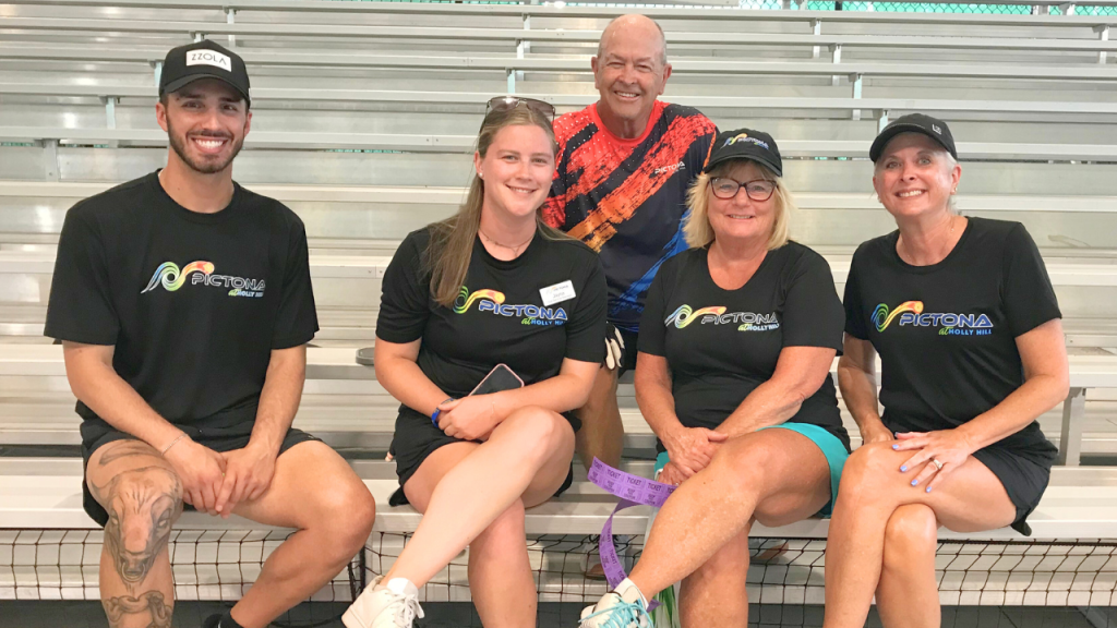 Pictona employees with Pictona T-Shirts sitting on bleachers, smiling at the camera. 