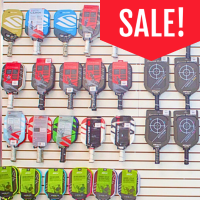photo of pickleball paddles on a wall with a large red SALE sign.